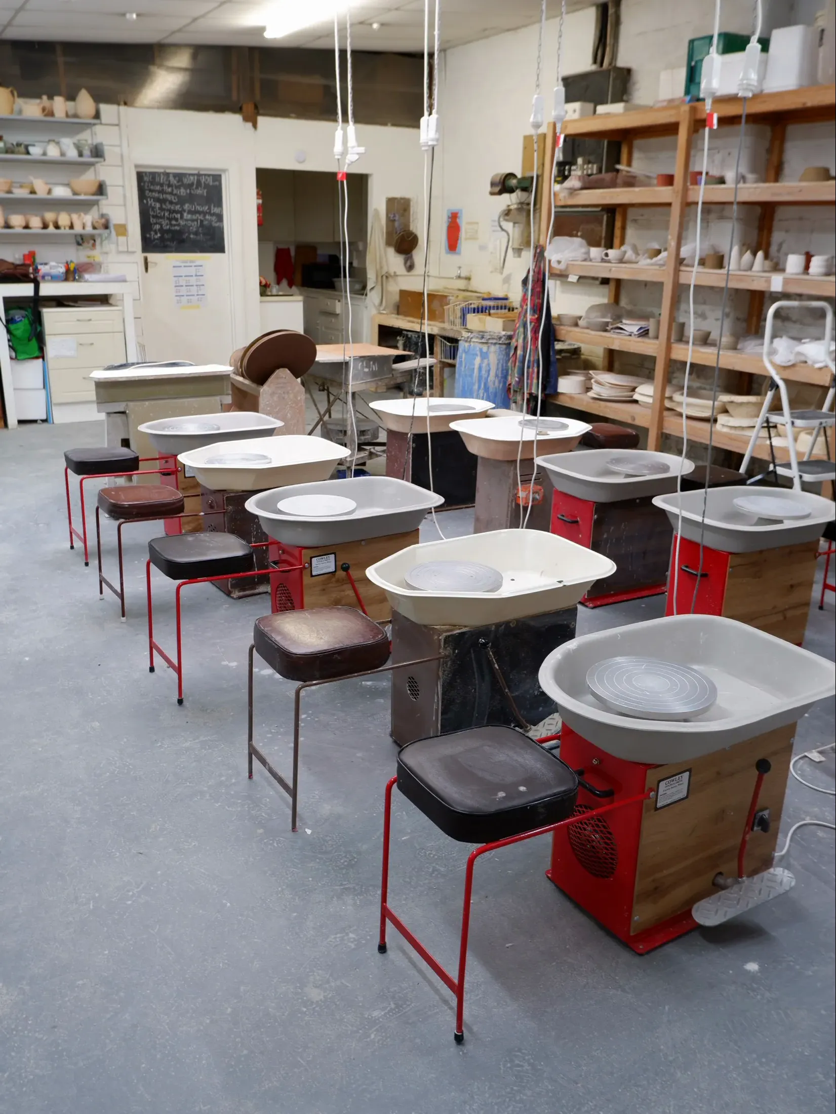 Pottery studio interior with wheels, shelves, and shared work space