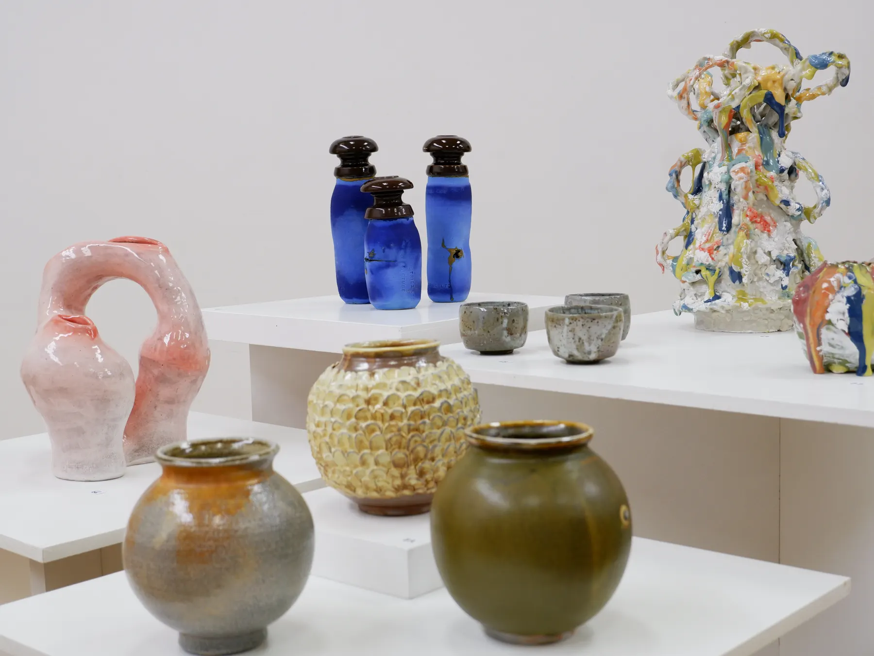 Ceramic pitchers and vessels displayed on white plinths in an exhibition space