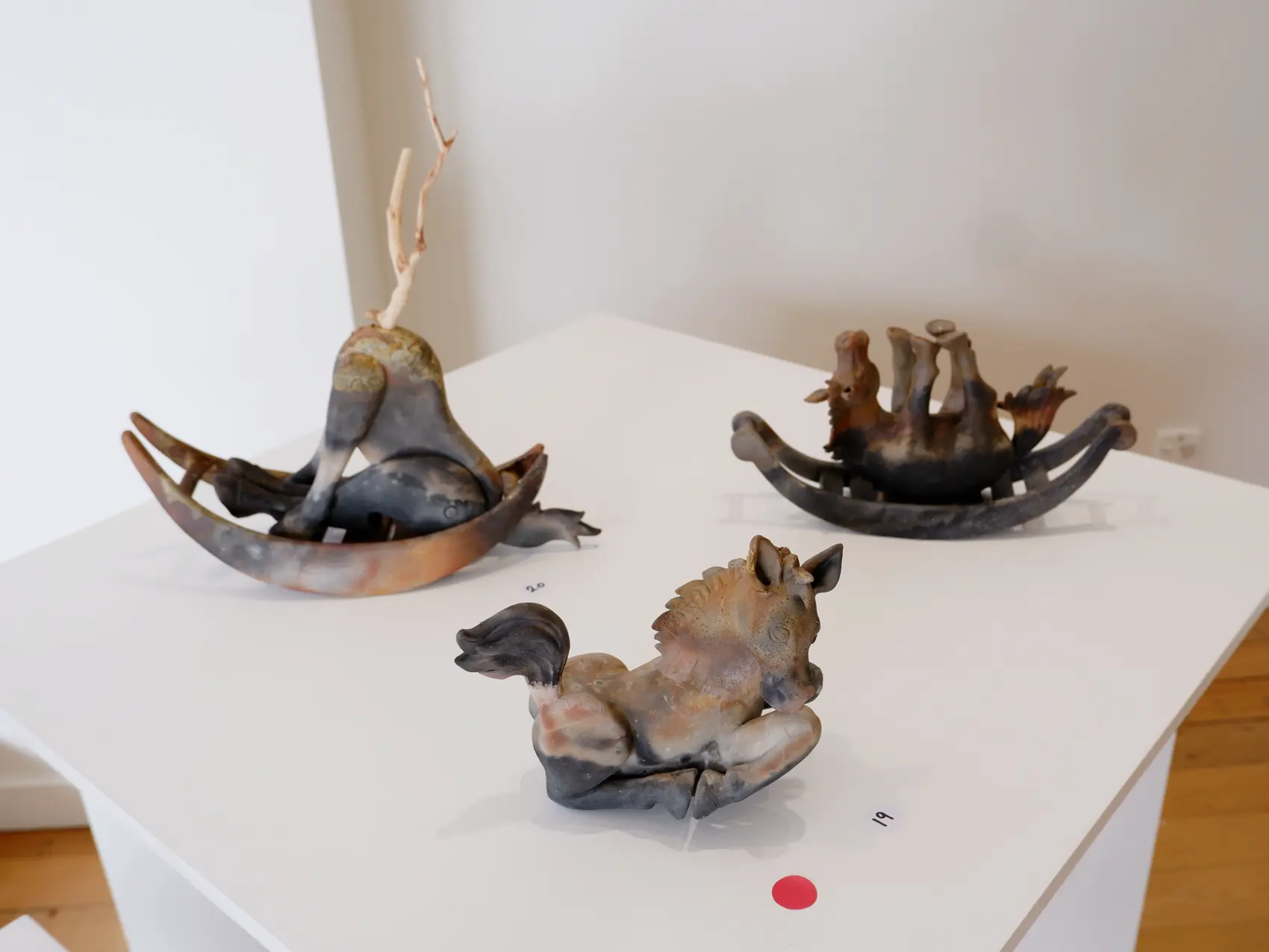 Ceramic figures and vessels displayed together on white plinths
